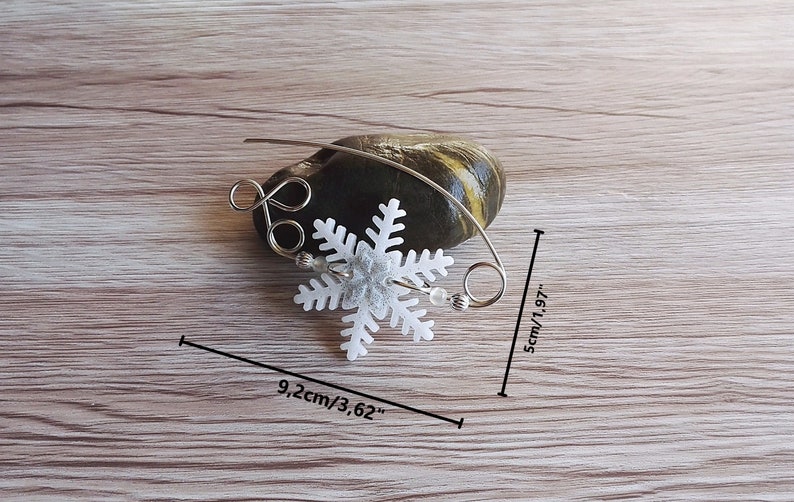 May include: A silver wire snowflake ornament with a white snowflake charm, measuring 5 cm by 9.2 cm.