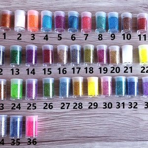 May include: Thirty-six small glass jars filled with various colors of glitter. The jars are arranged in rows and numbered 1 through 36.