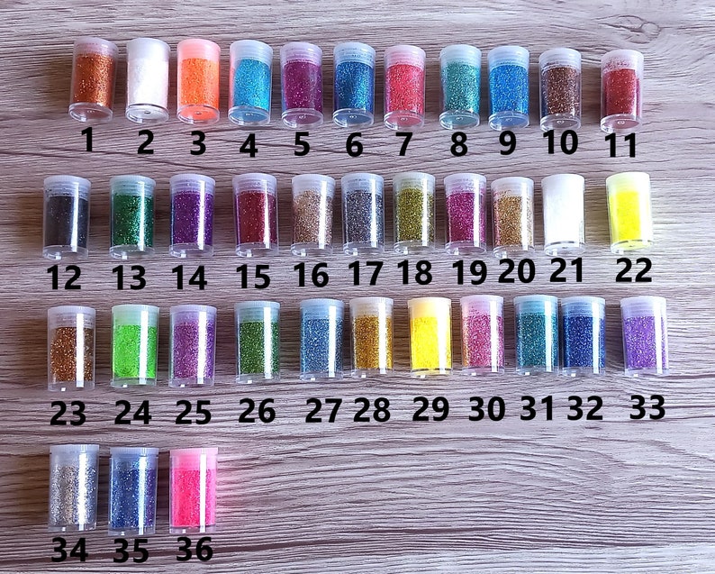 May include: Thirty-six small glass jars filled with various colors of glitter. The jars are arranged in rows and numbered 1 through 36.