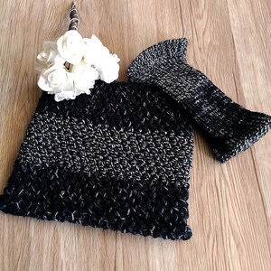 May include: A black and silver crocheted hat with a matching crocheted fingerless glove. The hat has a wide brim and the glove is long and narrow. The hat and glove are laid out on a wooden surface.