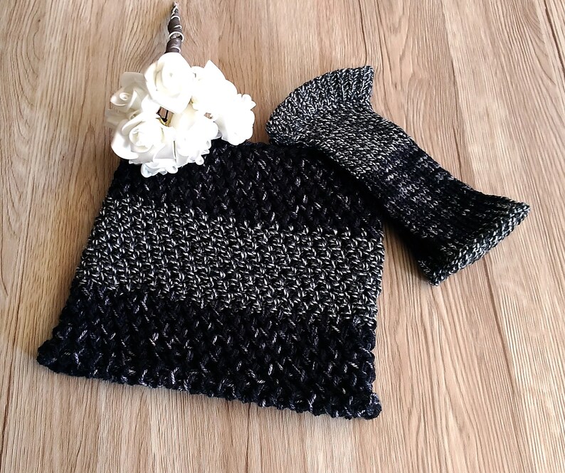 May include: A black and silver crocheted hat with a matching crocheted fingerless glove. The hat has a wide brim and the glove is long and narrow. The hat and glove are laid out on a wooden surface.