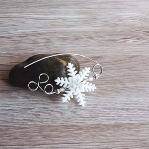 May include: A white snowflake charm attached to a silver wire with a silver loop. The charm is on a brown rock.