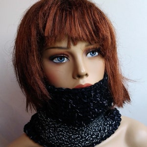 May include: A black and silver knitted neck warmer. The neck warmer is made of a soft, chunky yarn and has a simple, stylish design.