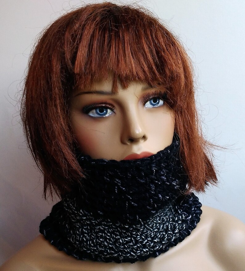 May include: A black and silver knitted neck warmer. The neck warmer is made of a soft, chunky yarn and has a simple, stylish design.