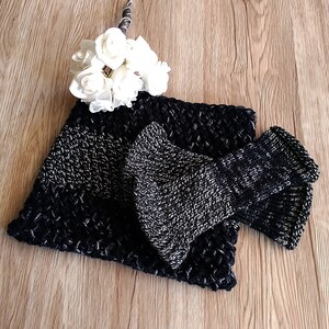 May include: A black and silver knitted scarf with a matching knitted bow. The scarf is folded in half and the bow is placed on top of the scarf.