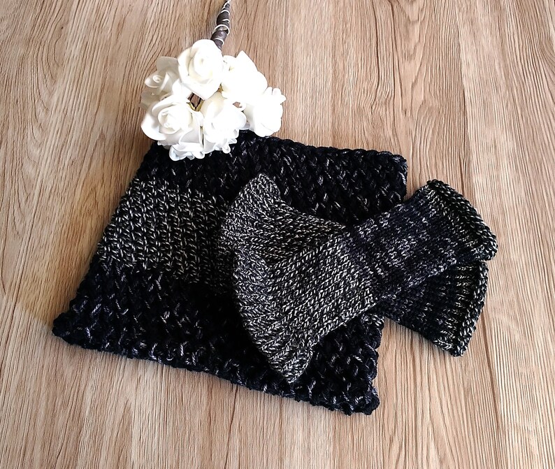 May include: A black and silver knitted scarf with a matching knitted bow. The scarf is folded in half and the bow is placed on top of the scarf.
