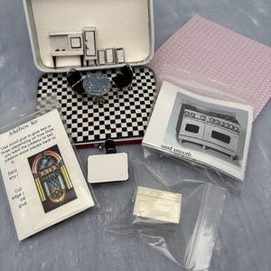 May include: A miniature dollhouse kit featuring a white metal suitcase containing a black and white checkered floor, a round table, two chairs, and small furniture pieces. Includes a jukebox kit, a stove instruction sheet, and a small white cabinet.