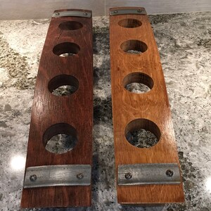 May include: Two wooden wine rack holders, each with four circular openings. One is a dark brown color, the other is a lighter brown. Both have metal accents and are made from reclaimed wood.