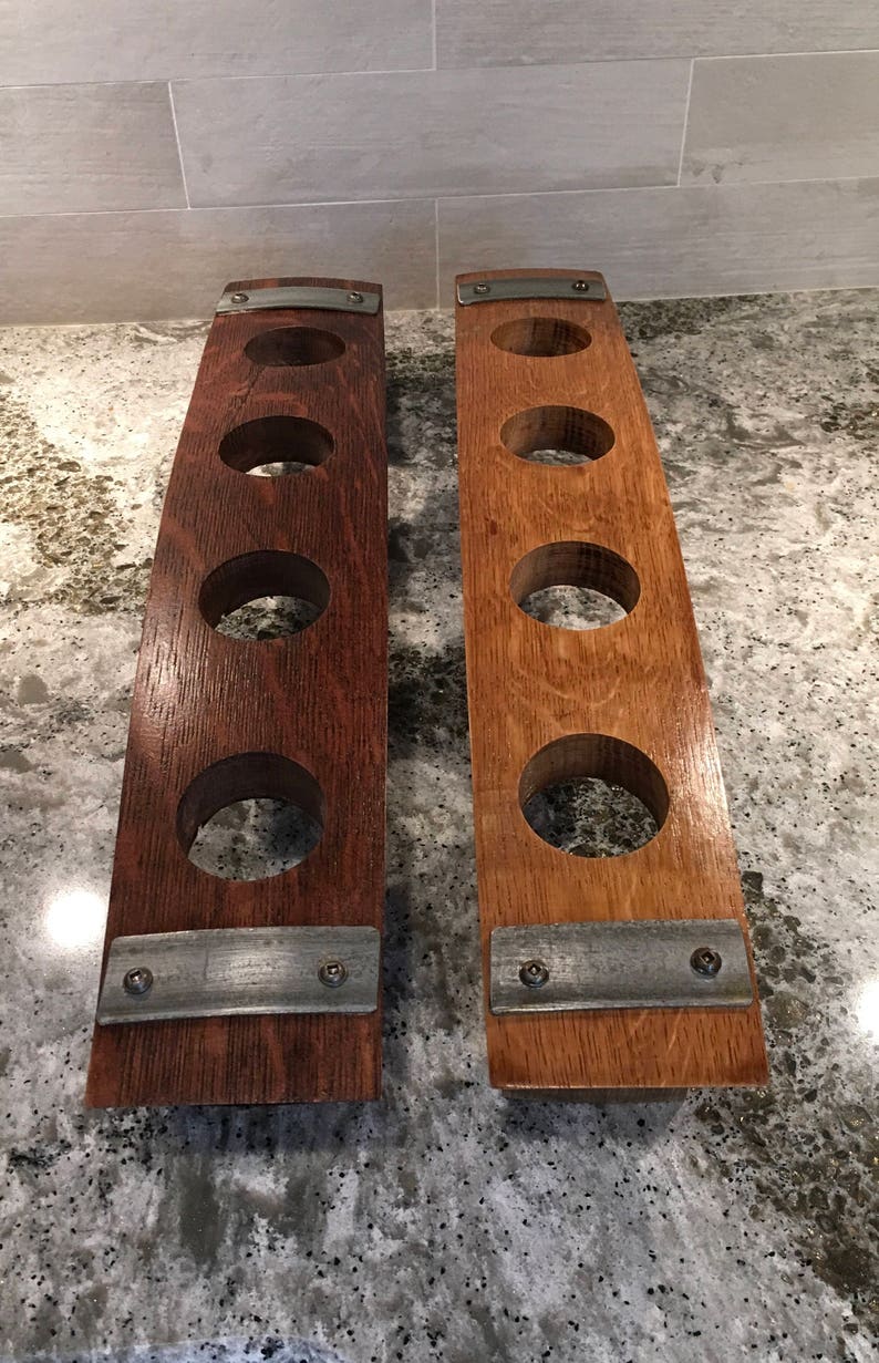 May include: Two wooden wine rack holders, each with four circular openings. One is a dark brown color, the other is a lighter brown. Both have metal accents and are made from reclaimed wood.