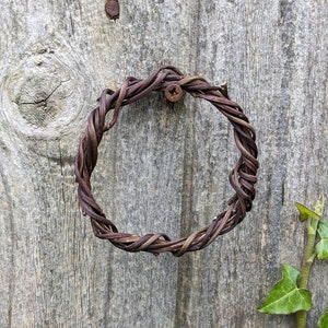 Peut inclure: Une couronne de brindilles brunes est fixée à une surface en bois vieilli avec un clou rouillé. Une vigne verte avec des feuilles pousse sur le côté droit de l'image.