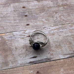 May include: A silver wire ring with a black bead in the center.