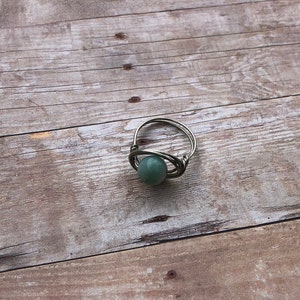 May include: A silver wire ring with a green gemstone. The ring is on a wooden surface.