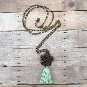 Könnte beinhalten: Eine goldene Kettenkette mit einem großen, verzierten, bronzenen Blumenanhänger und einem hellgrünen Quasten.