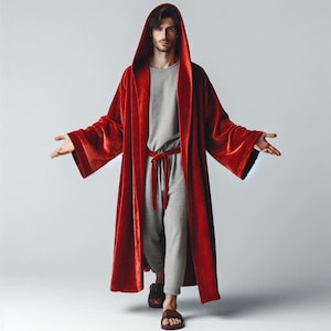 May include: A person wearing a long, red robe with a hood. The robe is cinched at the waist with a belt. The person is standing with their arms outstretched.