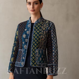 May include: A woman wearing a navy blue dress and a patterned jacket. The jacket features a mix of blue, green, and gold floral and geometric designs. The jacket has a mandarin collar and is trimmed with white piping. The text "KAFTANBUZZ" is visible.