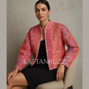 May include: A pink and coral quilted jacket with floral and paisley patterns. The jacket has a mandarin collar, a button closure, and a contrasting trim. The text "KAFTANBUZZ" is visible on the jacket.