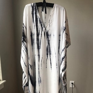 May include: White and black tie-dye kaftan with a V-neck and short sleeves. The kaftan is hanging on a hanger.