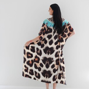 K&ouml;nnte beinhalten: Eine lange, flie&szlig;ende Kaftan mit Leopardenmuster und einem blauen und wei&szlig;en Blumendesign am Ausschnitt. Die Kaftan wird von einer Person mit langen schwarzen Haaren getragen und von hinten gezeigt.