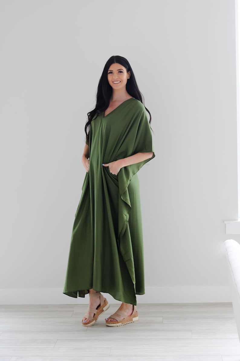 May include: A long, flowing green maxi dress with a V-neck and short sleeves. The dress has a relaxed fit and features pockets on the sides.