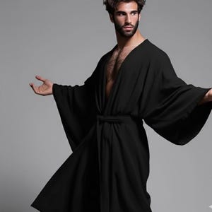 May include: A black robe with wide sleeves and a matching belt. The robe has a V-neck design and is made of a soft, flowing fabric. The model is wearing the robe open, revealing the chest.