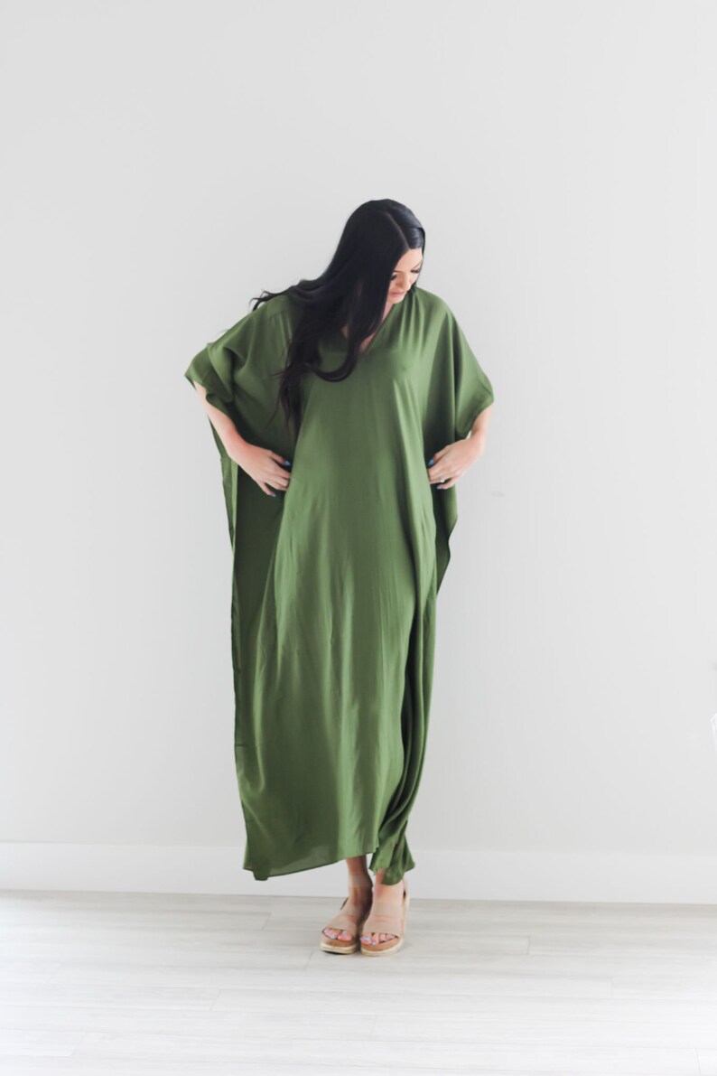 May include: A long, flowing green maxi dress with a V-neckline and short sleeves. The dress is made of a soft, lightweight fabric and has a relaxed fit.