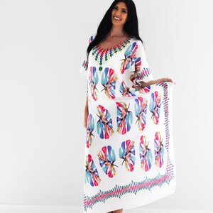 May include: White maxi dress with a colourful floral print and a jeweled neckline. The dress has a flowing silhouette and a relaxed fit.