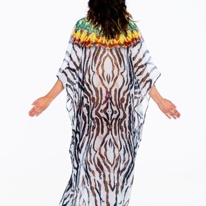 May include: A flowing, sheer caftan with a zebra stripe pattern in black and white. The neckline features a colorful, patterned trim in green, yellow, and orange. The garment is worn with high-heeled sandals.