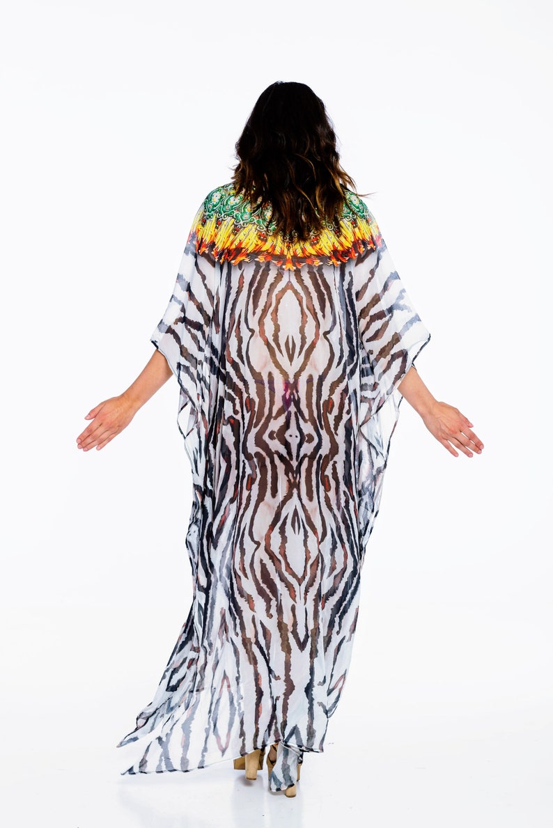 May include: A flowing, sheer caftan with a zebra stripe pattern in black and white. The neckline features a colorful, patterned trim in green, yellow, and orange. The garment is worn with high-heeled sandals.
