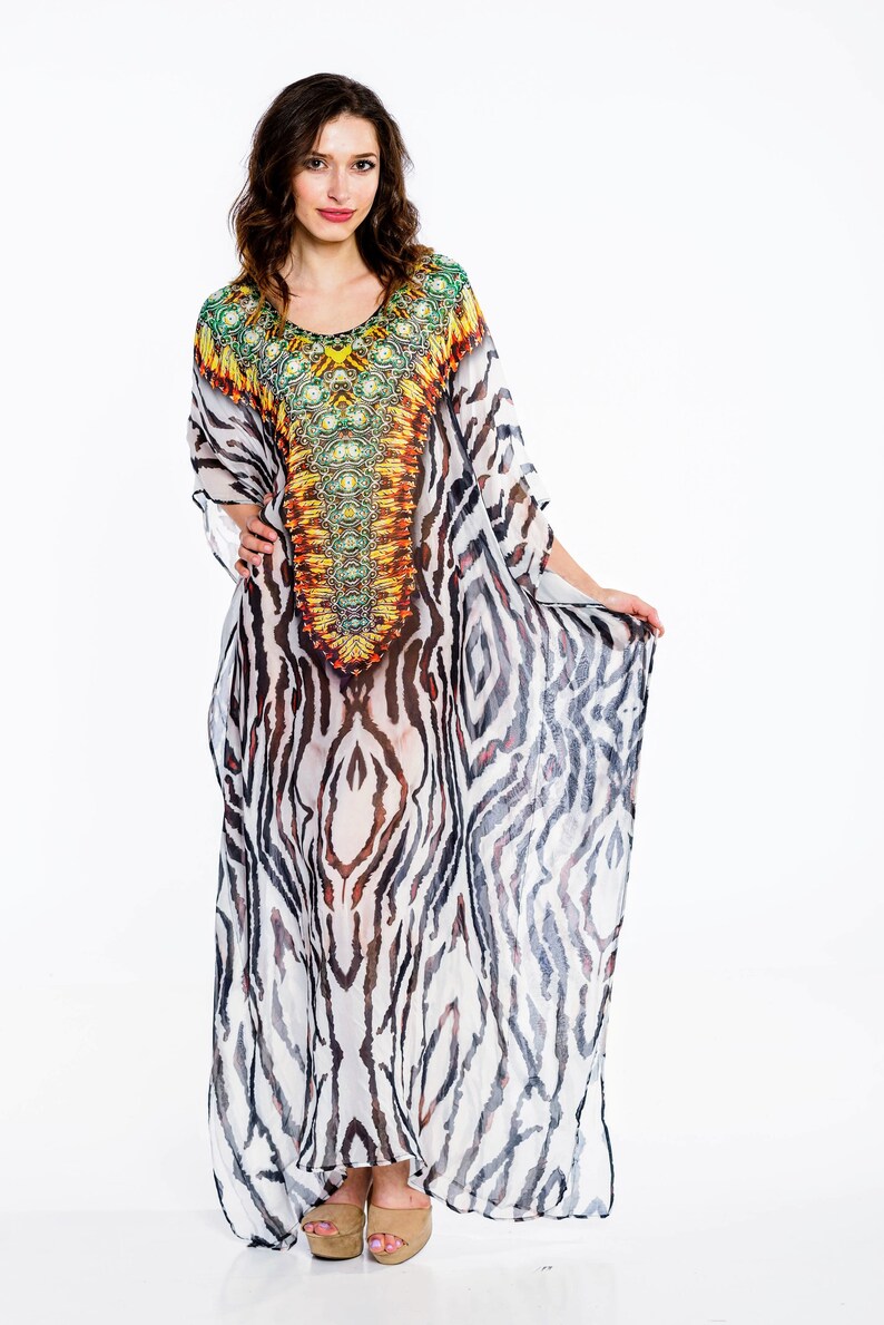 May include: A long, flowing kaftan dress with a vibrant, patterned bodice in shades of green, yellow, and orange. The dress features a zebra stripe pattern in black and white. The model is wearing beige platform sandals.