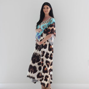 K&ouml;nnte beinhalten: Eine schwangere Person tr&auml;gt ein langes, flie&szlig;endes Maxikleid mit Leopardenmuster. Das Kleid hat ein blaues und t&uuml;rkisfarbenes Oberteil mit bunten Verzierungen. Die Person tr&auml;gt braune Sandalen.