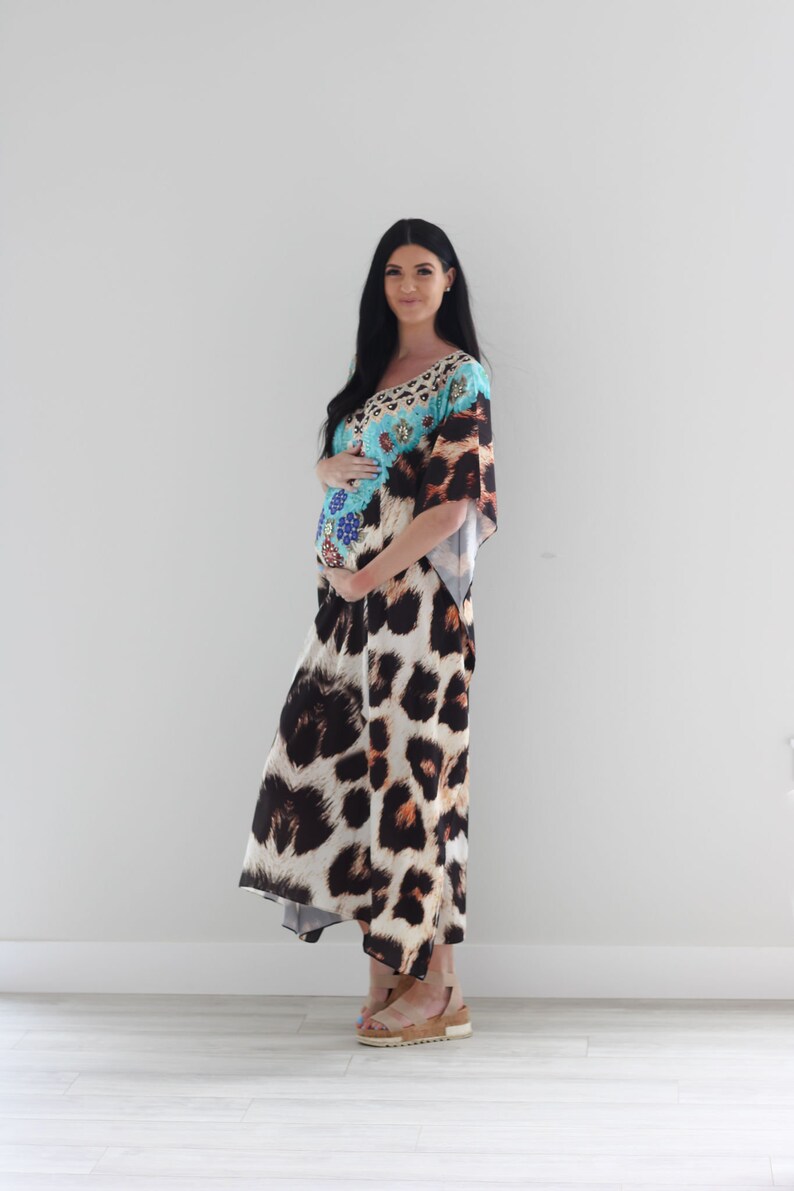 K&ouml;nnte beinhalten: Eine schwangere Person tr&auml;gt ein langes, flie&szlig;endes Maxikleid mit Leopardenmuster. Das Kleid hat ein blaues und t&uuml;rkisfarbenes Oberteil mit bunten Verzierungen. Die Person tr&auml;gt braune Sandalen.