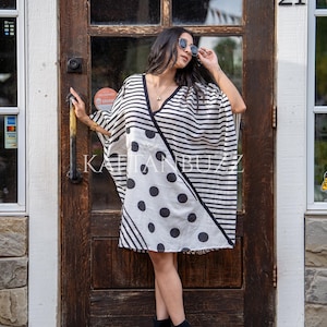 May include: A black and white patterned wrap dress with a V-neck. The dress features horizontal stripes and large polka dots. The dress is worn with black ankle boots.