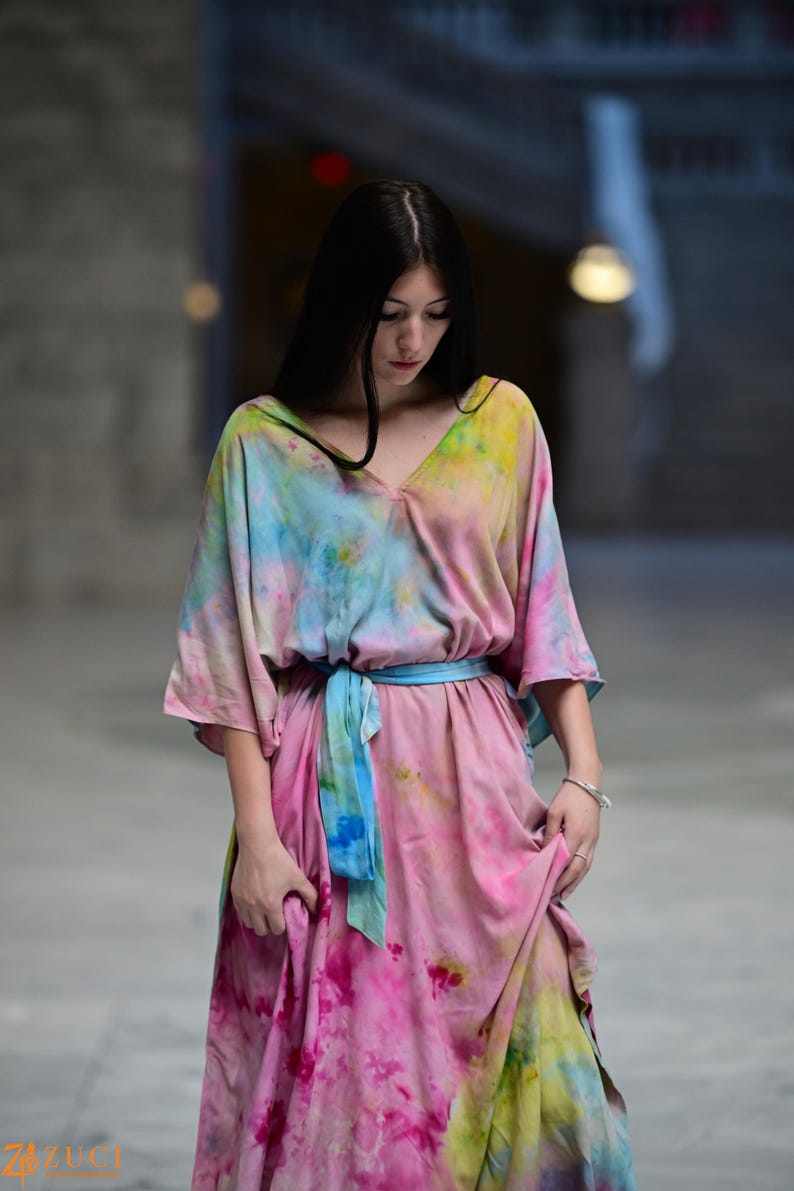 Może przedstawiać: Sukienka maxi w stylu tie-dye z dekoltem w serek i kr&oacute;tkimi rękawami. Sukienka ma r&oacute;żową, niebieską i ż&oacute;łtą kolorystykę, z niebieskim pasem wiązanym w talii. Sukienka jest wykonana z miękkiej, zwiewnej tkaniny.