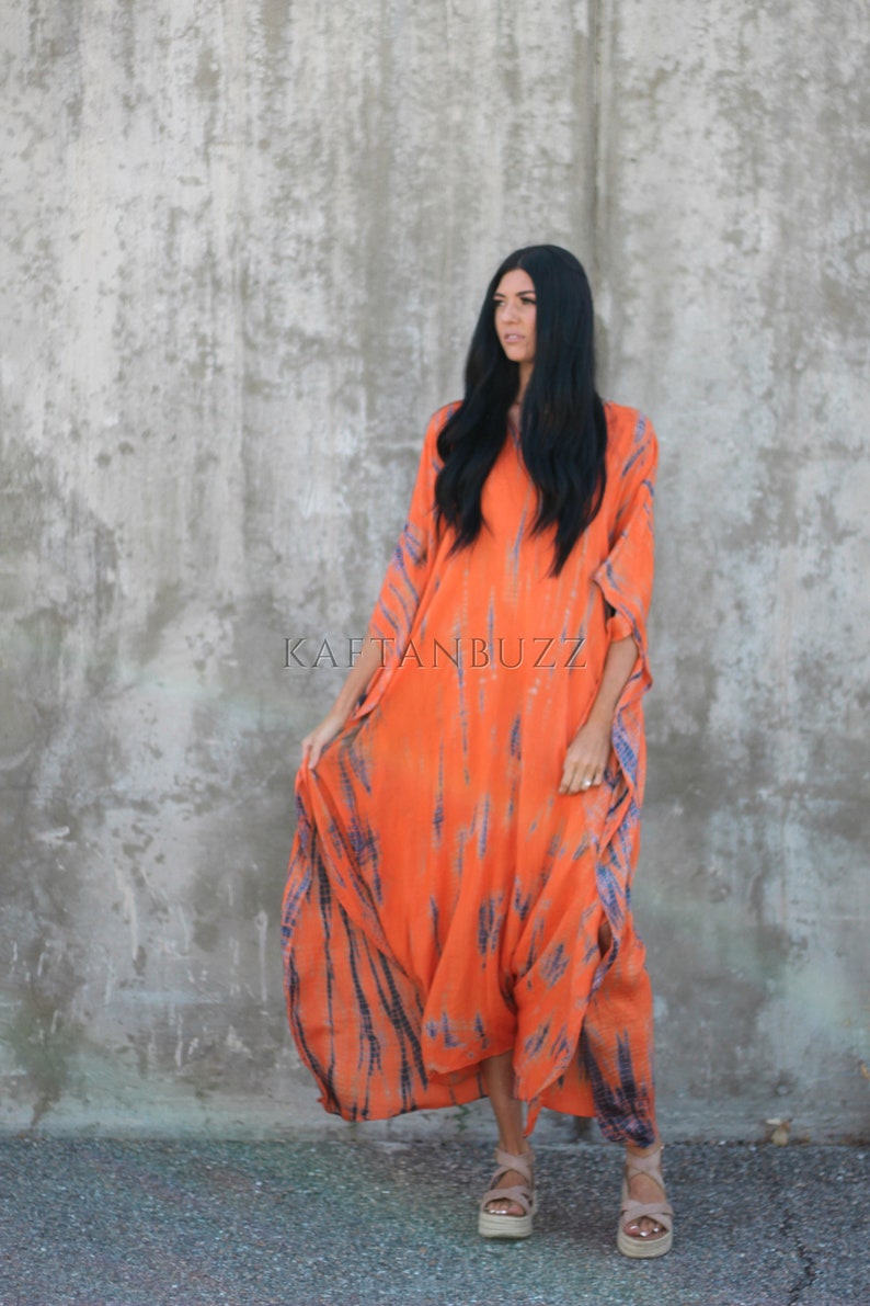 Puede incluir: Una mujer lleva un vestido largo de kaft&aacute;n de color naranja y azul con estampado tie-dye. El vestido tiene un corte holgado y fluido, ideal para un look casual de verano. El vestido est&aacute; hecho de una tela suave y c&oacute;moda, perfecto para un d&iacute;a en la playa o una noche de fiesta con amigos. El vestido est&aacute; disponible en una variedad de colores y tallas.