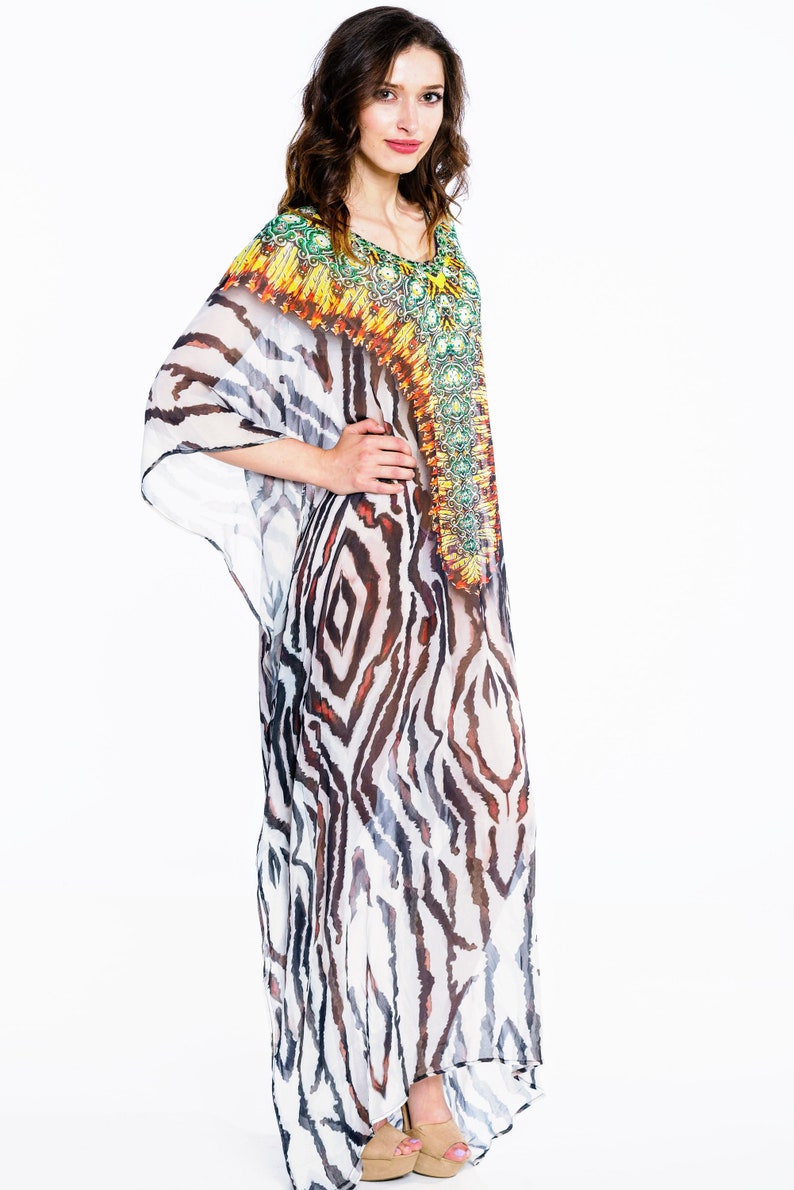 May include: A flowing, sheer caftan dress with a zebra stripe pattern in black, white, and brown. The neckline and upper chest area feature a colorful, ornate design with green, yellow, and orange accents. The dress is floor-length.