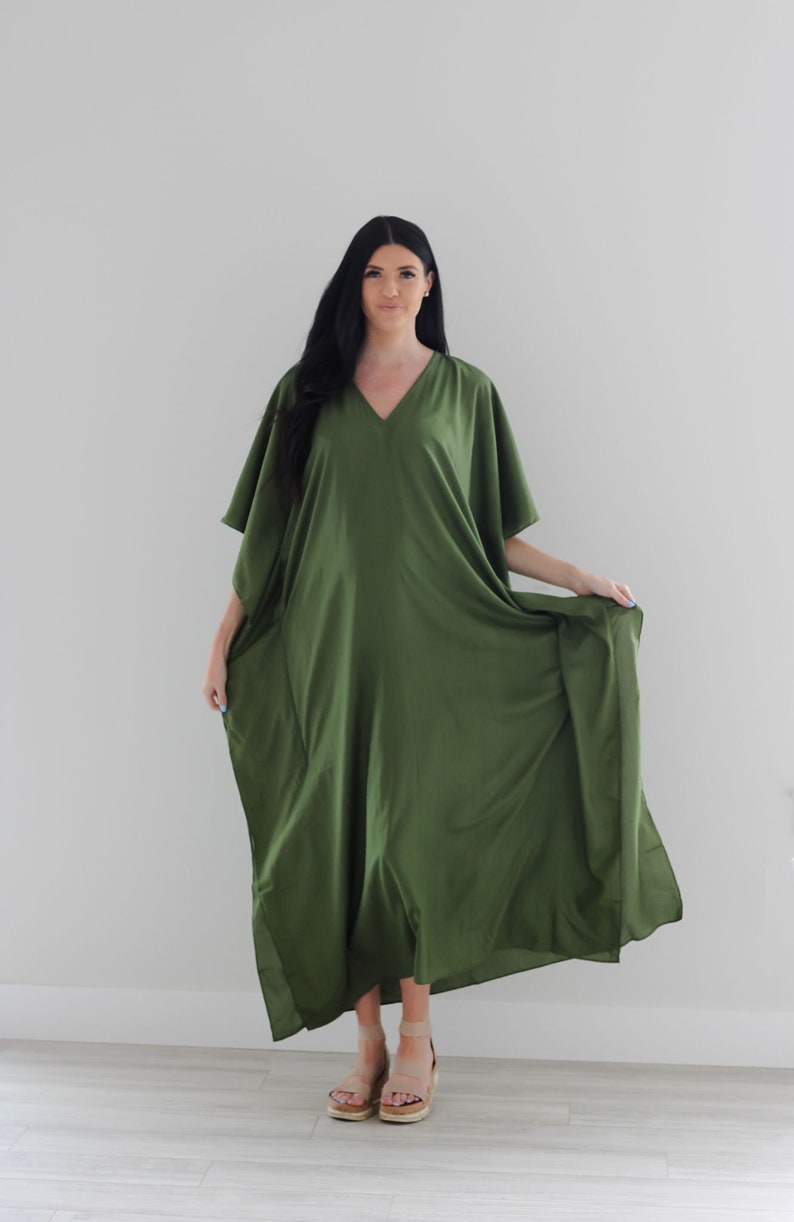 May include: A long, flowing green kaftan dress with a V-neckline and short sleeves. The dress is made of a soft, lightweight fabric and has a relaxed fit.