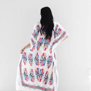 May include: White maxi dress with a colourful tropical leaf print. The dress has a loose, flowing silhouette and a V-neckline.