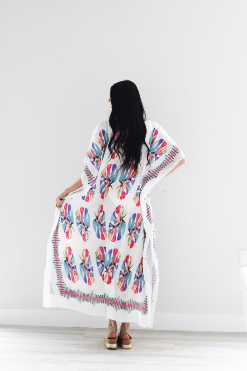 May include: White maxi dress with a colourful tropical leaf print. The dress has a loose, flowing silhouette and a V-neckline.