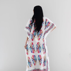 May include: White maxi dress with a colourful tropical leaf print. The dress has a loose, flowing silhouette and a V-neckline.