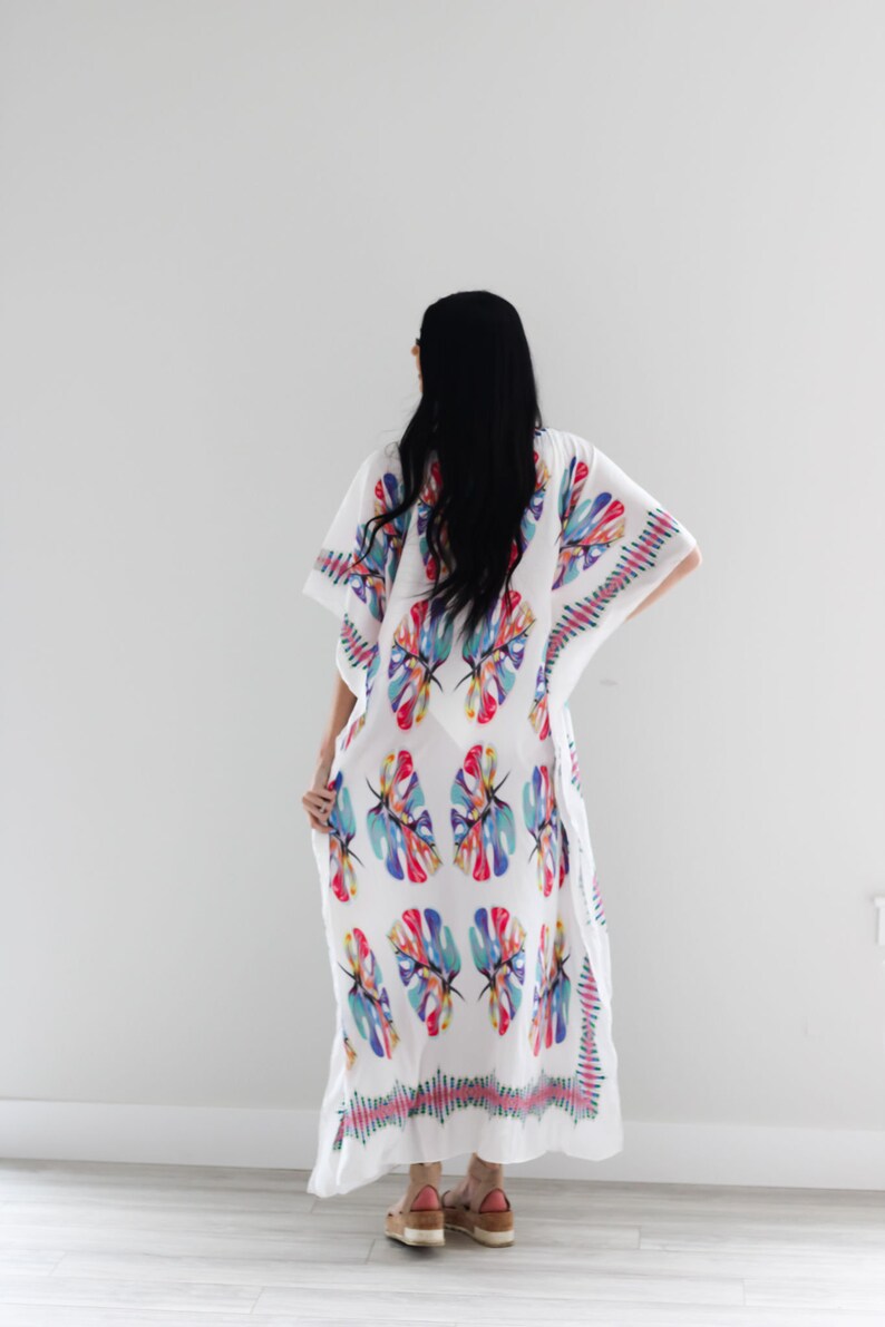 May include: White maxi dress with a colourful tropical leaf print. The dress has a loose, flowing silhouette and a V-neckline.