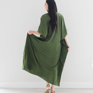 May include: A long, flowing green maxi dress with a loose, comfortable fit. The dress has a V-neckline and short sleeves. The model is wearing the dress with a pair of brown platform sandals.