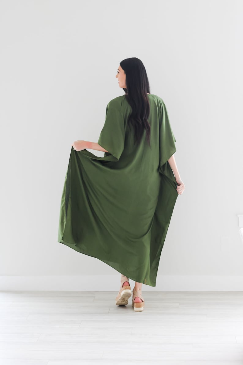 May include: A long, flowing green maxi dress with a loose, comfortable fit. The dress has a V-neckline and short sleeves. The model is wearing the dress with a pair of brown platform sandals.