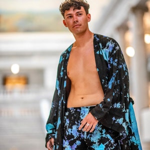 May include: A person wearing a black and blue tie-dye robe and matching shorts. The robe is open, revealing the person's bare chest. The person is standing in a large, open space with a white tiled floor.