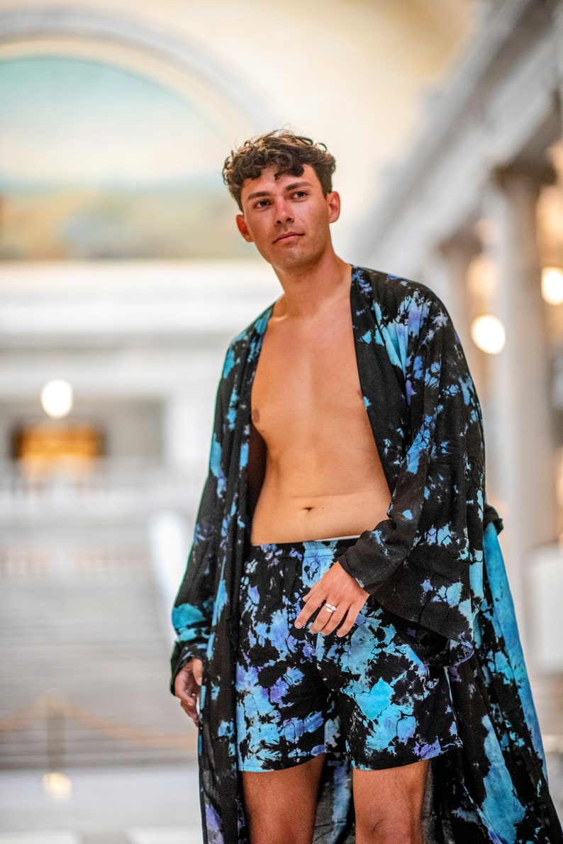 May include: A person wearing a black and blue tie-dye robe and matching shorts. The robe is open, revealing the person's bare chest. The person is standing in a large, open space with a white tiled floor.