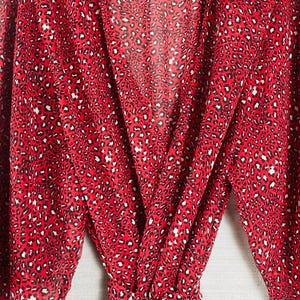 May include: A red wrap dress with a leopard print pattern. The dress features long sleeves and a tie waist. The text "KAFTANBUZZ" is visible on the label. The dress is made of a lightweight fabric.