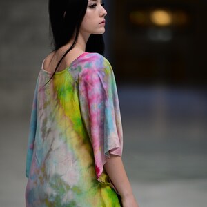 Może przedstawiać: Kolorowa sukienka tie-dye z okrągłym dekoltem i kr&oacute;tkimi rękawami. Sukienka ma żywą mieszankę r&oacute;żowych, ż&oacute;łtych, zielonych i niebieskich odcieni. Modelka jest widoczna z tyłu i z boku, prezentując płynny kr&oacute;j sukienki.