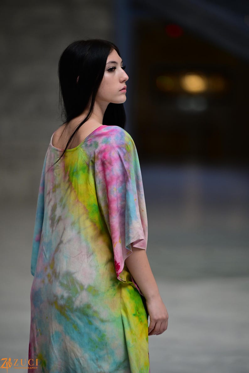 Może przedstawiać: Kolorowa sukienka tie-dye z okrągłym dekoltem i kr&oacute;tkimi rękawami. Sukienka ma żywą mieszankę r&oacute;żowych, ż&oacute;łtych, zielonych i niebieskich odcieni. Modelka jest widoczna z tyłu i z boku, prezentując płynny kr&oacute;j sukienki.