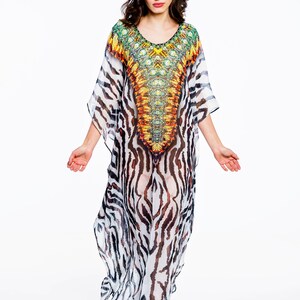 May include: A flowing, floor-length caftan dress with a vibrant, patterned bodice and zebra-striped skirt. The dress features a scoop neckline and wide sleeves. The bodice showcases a colorful design with shades of yellow, orange, and green.
