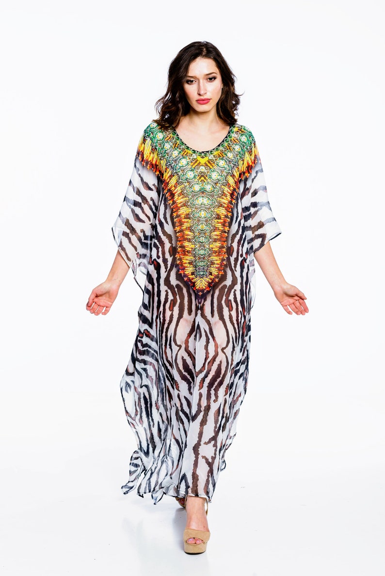 May include: A flowing, floor-length caftan dress with a vibrant, patterned bodice and zebra-striped skirt. The dress features a scoop neckline and wide sleeves. The bodice showcases a colorful design with shades of yellow, orange, and green.