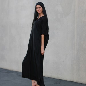 May include: A woman wearing a long black maxi dress with a v-neck and short sleeves. She is wearing nude platform sandals.